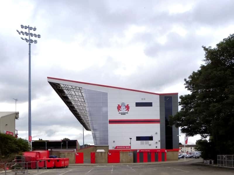 Foto de archivo: la tribuna sur del estadio Kingsholm, blanca con detalles rojos y el escudo de Gloucester Rugby, en un día nublado