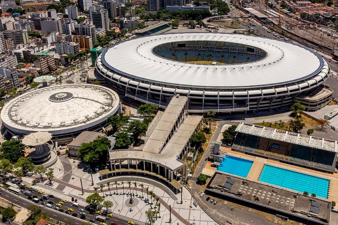 Vista aérea del estadio Maracaná de Río de Janeiro, con su techo blanco circular, rodeado de edificios, un gimnasio y un parque acuático con dos piletas