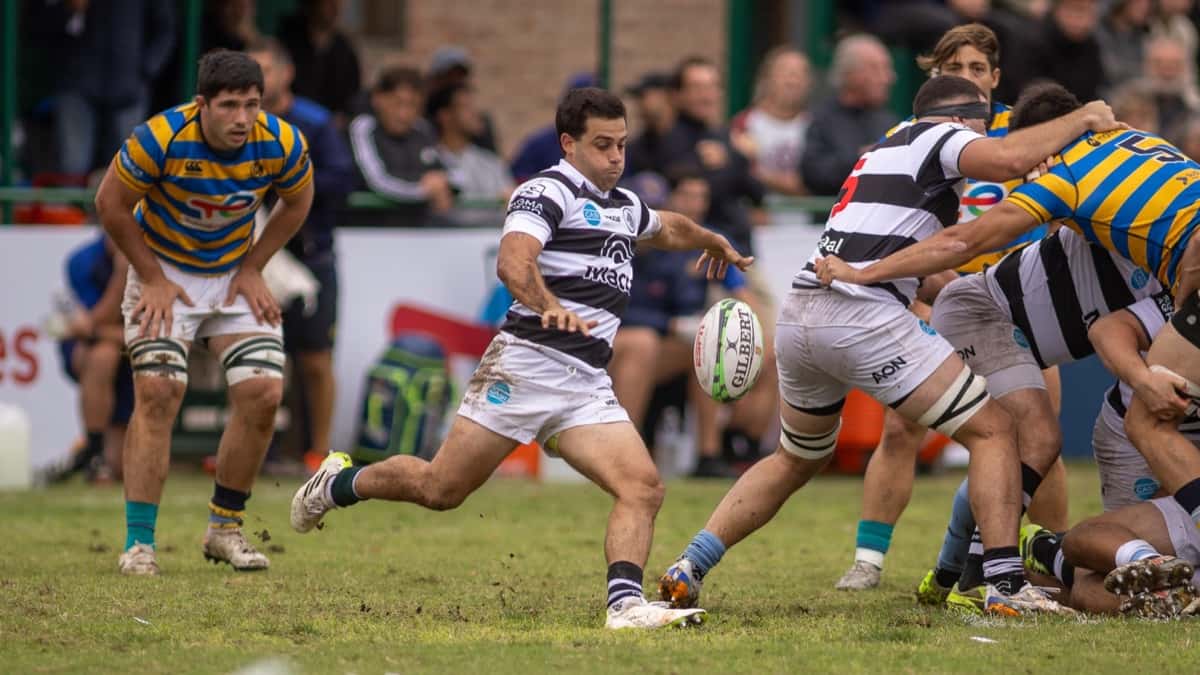 Foto de archivo: un jugador del CASI, con camiseta a rayas blancas y negras, patea la pelota desde el pie de un ruck ante un rival de camiseta a rayas azules y amarillas