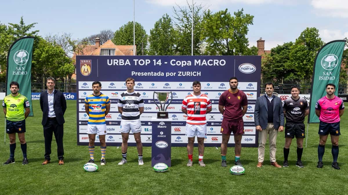 Jugadores de Hindú, CASI, Alumni y Newman, cada uno con la camiseta de su club, posan junto a la copa del URBA Top 14 en la cancha del CASI, con dirigentes y árbitros a los costados