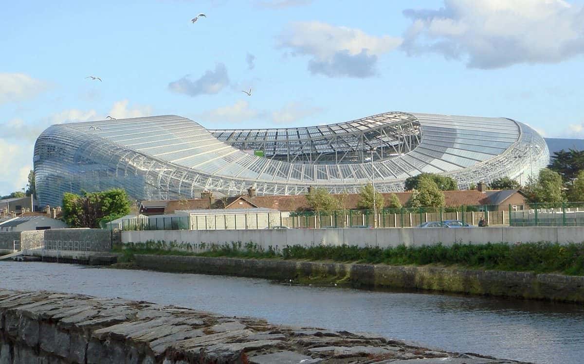 Imagen del estadio: el Aviva Stadium de Dublín, con su techo curvo de vidrio y acero, visto desde la orilla del río Dodder