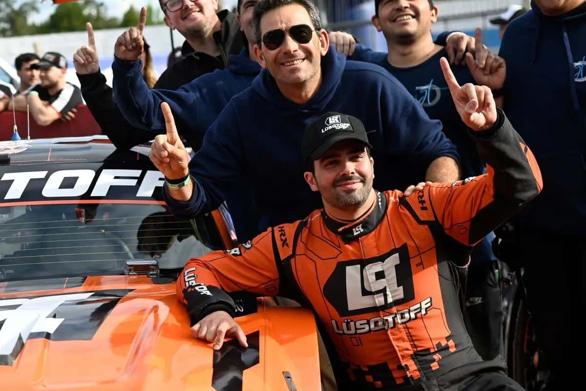 Mauricio Lambiris, con buzo naranja, festeja con el dedo índice en alto junto a su Ford Mustang y a su equipo después de la clasificación del TC en Rosario
