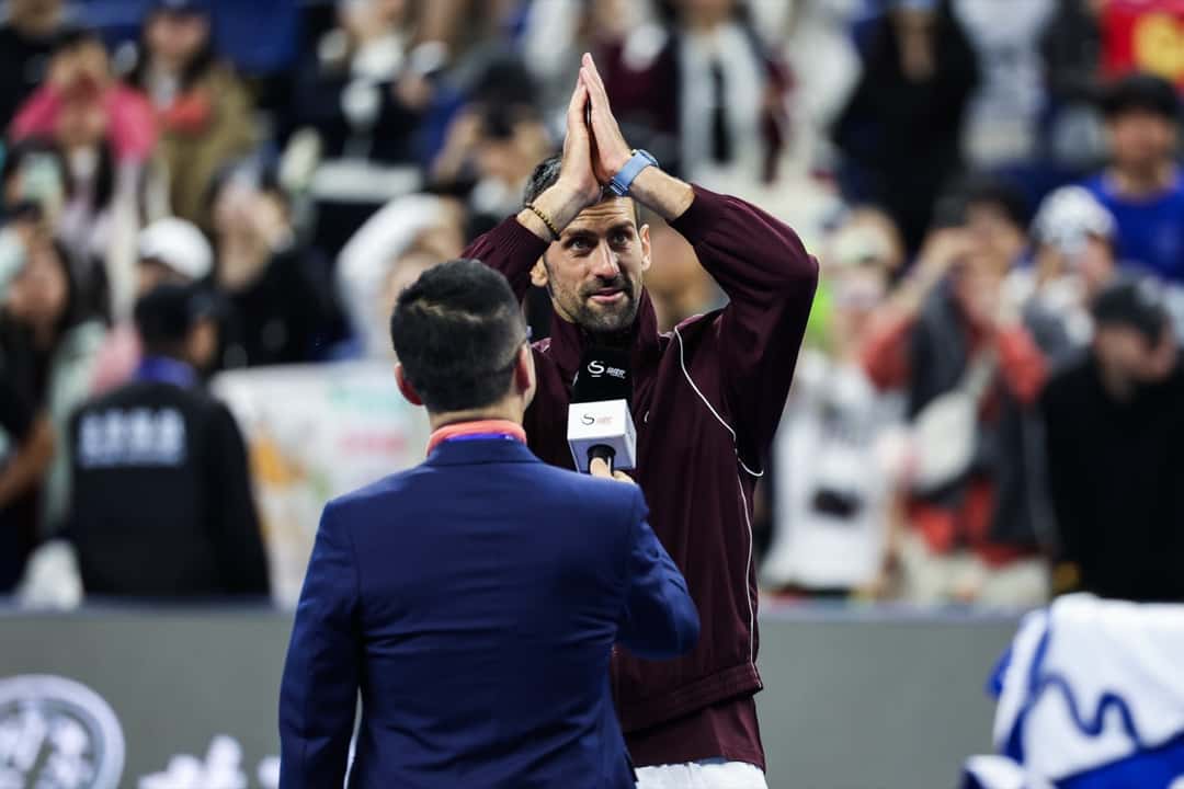Novak Djokovic junta las manos para agradecerle al público durante una entrevista en la cancha del China Open 2026