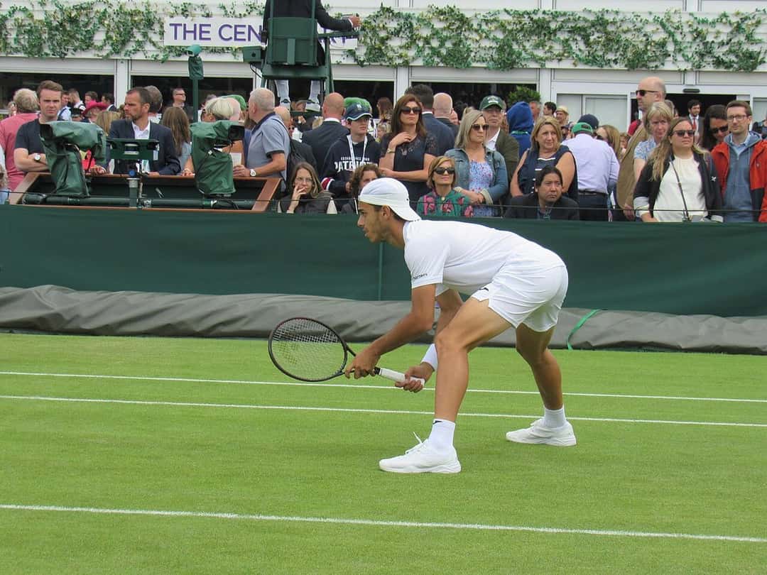 Foto de archivo: Francisco Cerúndolo, de blanco y con gorra, en posición de devolución en una cancha de césped de Wimbledon, con público detrás
