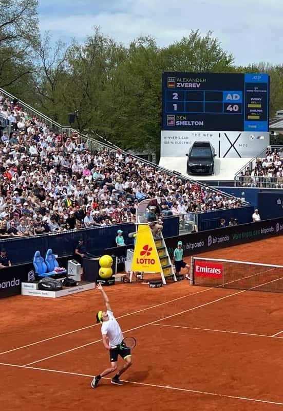 Foto de archivo: Alexander Zverev, de blanco y negro, saca en una cancha de polvo de ladrillo ante una tribuna llena, con el tablero que muestra su partido contra Ben Shelton