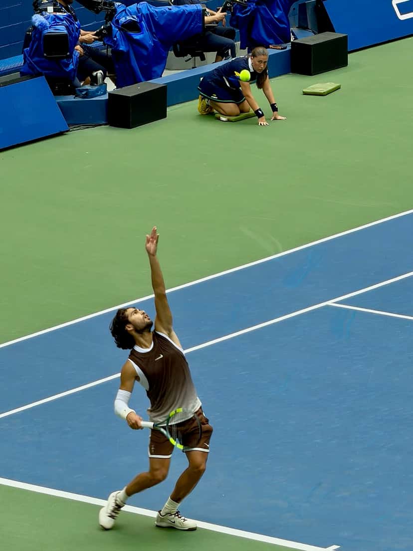 Foto de archivo: Carlos Alcaraz, con musculosa marrón y blanca, saca en una cancha dura azul del US Open 2026