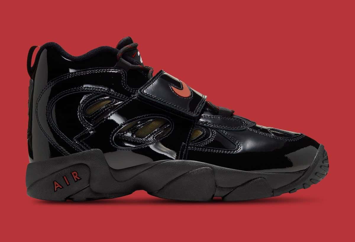 Nike Air Diamond Turf 2 en charol negro con Swoosh y detalles rojos, de perfil sobre fondo rojo