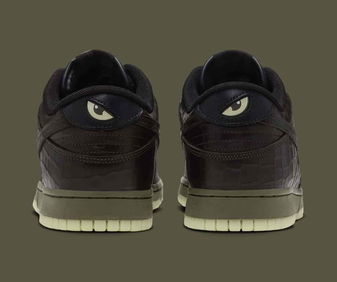 Talón del Nike Dunk Low Shibuya Halloween visto desde atrás, con un ojo verde claro en cada talón, cuero negro texturado, mediasuela verde oliva y suela verde clara