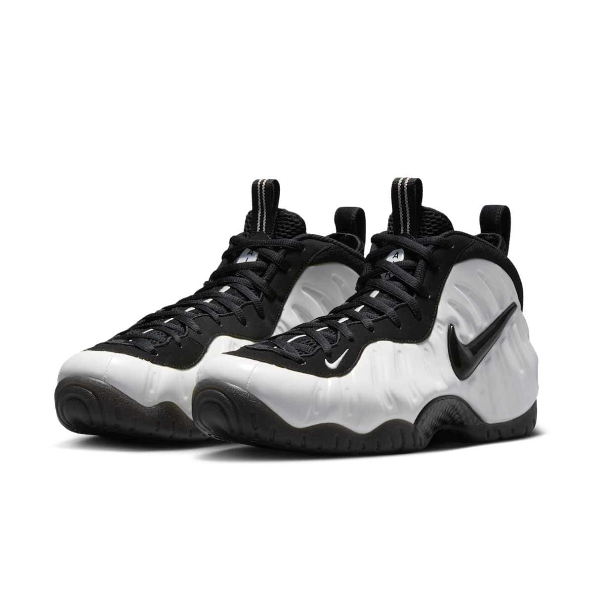Par de Nike Air Foamposite Pro Premium Summit White en vista de tres cuartos, con carcasa blanca moldeada, Swoosh negro brillante, cordones negros y suela negra