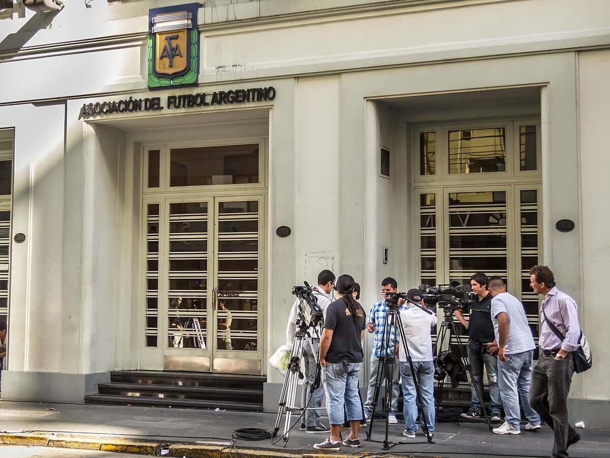 La entrada de la sede de la AFA en Buenos Aires, con el escudo y el nombre de la Asociación del Fútbol Argentino sobre la puerta y periodistas con cámaras en la vereda; foto de archivo de 2013 (foto: Barcex, Wikimedia Commons, licencia CC BY-SA 3.0)