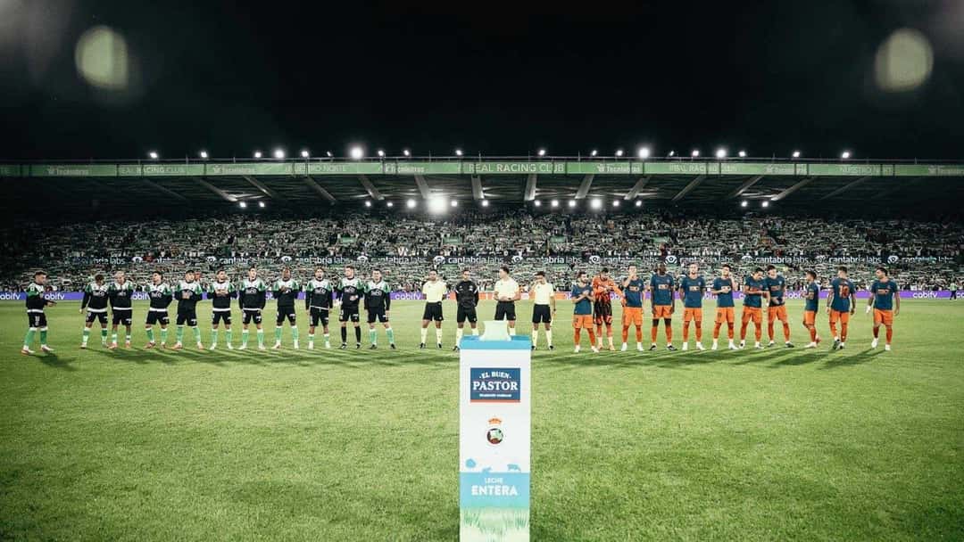 Los dos equipos formados en el campo de El Sardinero antes del partido, con Racing de verde y negro a la izquierda, la terna arbitral en el medio y el Valencia a la derecha, ante las tribunas llenas (foto: prensa Valencia CF)