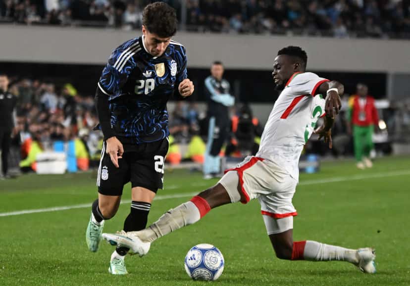 Un jugador de la Selección Argentina con la camiseta 28 conduce la pelota ante la barrida de un defensor de Burkina Faso