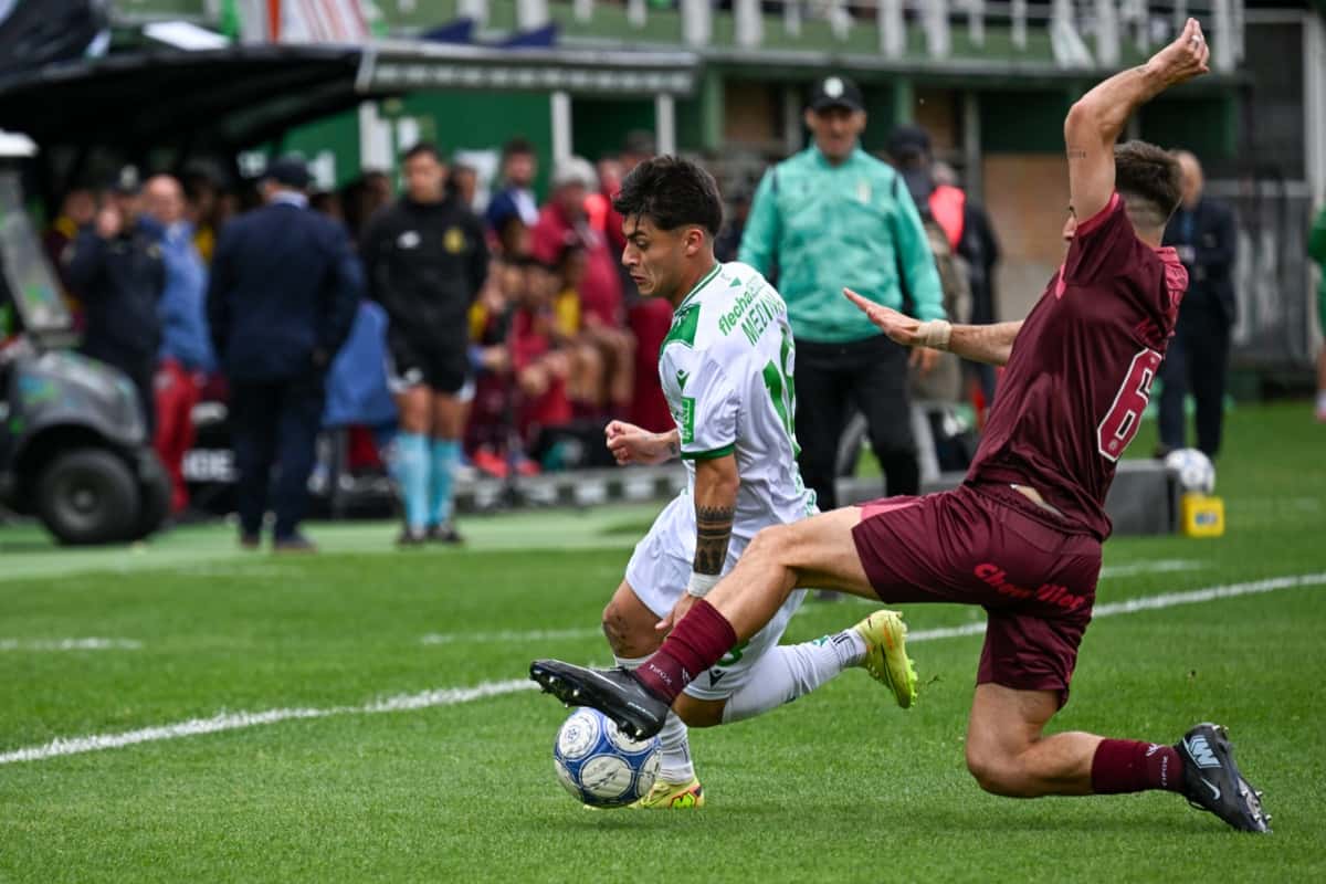Un jugador de Banfield, con la camiseta blanca y verde, protege la pelota ante la barrida de un defensor de Lanús, de granate, en el clásico del Sur del sábado 24 en el Florencio Sola (foto: prensa Liga Profesional de Fútbol)