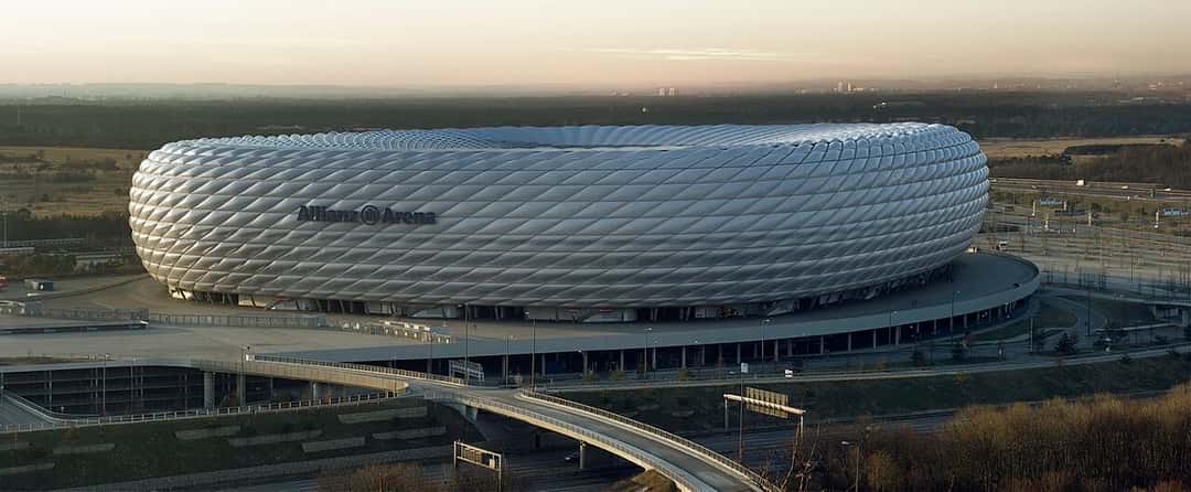 El exterior del Allianz Arena de Múnich, con su fachada de paneles blancos, visto desde lejos con luz de día; foto de archivo de enero de 2008 (foto: Richard Bartz, Wikimedia Commons, licencia CC BY-SA 2.5)