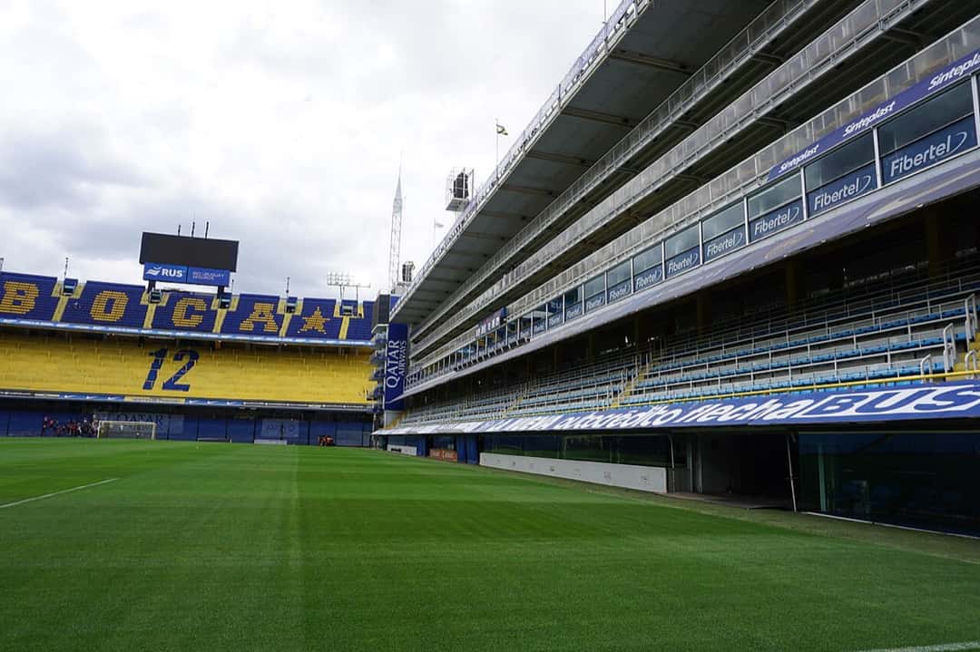 El campo de juego de La Bombonera con la tribuna que muestra el nombre de Boca y el número 12 en sus butacas amarillas y azules, y los palcos a la derecha, en un día nublado; foto de archivo de 2019 (foto: Arzam879, Wikimedia Commons, licencia CC BY-SA 4.0)