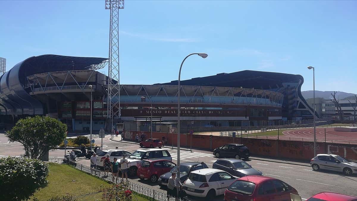 El estadio de Balaídos, en Vigo, visto desde la calle, con una torre de iluminación y autos estacionados frente a la tribuna; foto de archivo de junio de 2019 (foto: Rion Tools, Wikimedia Commons, licencia CC BY-SA 4.0)