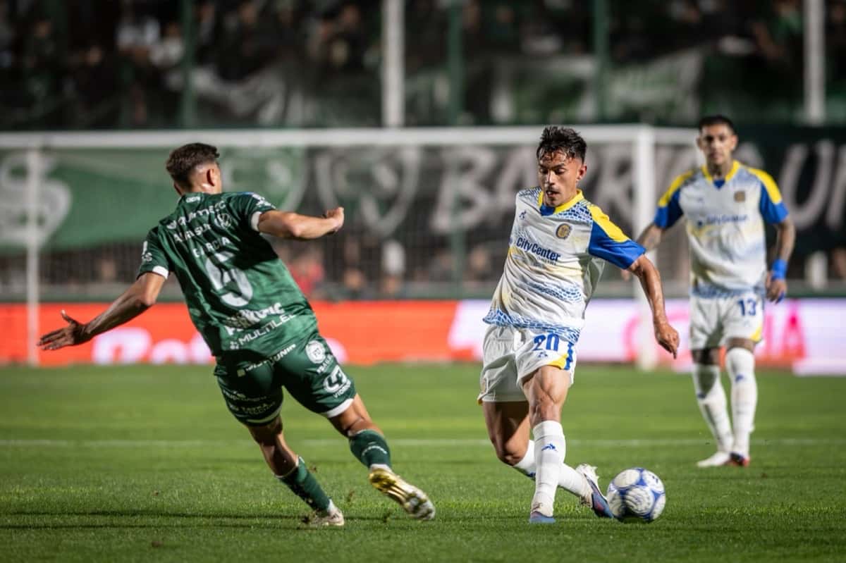 Un jugador de Rosario Central, con la camiseta blanca con detalles azules y amarillos, maneja la pelota presionado por un jugador de Sarmiento de camiseta verde, en el partido del viernes 30 de octubre en Junín (foto: prensa Liga Profesional de Fútbol)