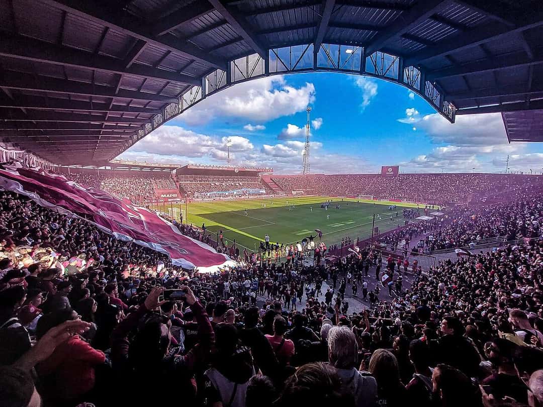 El estadio de Lanús lleno, con las tribunas teñidas de granate y la cancha iluminada bajo un cielo con nubes; foto de archivo de abril de 2025 (foto: 1915CAL, Wikimedia Commons, licencia CC BY 4.0)