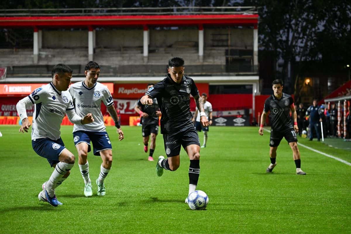 Jugadores con camiseta negra y con camiseta blanca y azul pelean la pelota en un partido del Torneo Clausura 2026, con una tribuna roja de fondo; foto de archivo de octubre de 2026 (foto: prensa Liga Profesional de Fútbol)