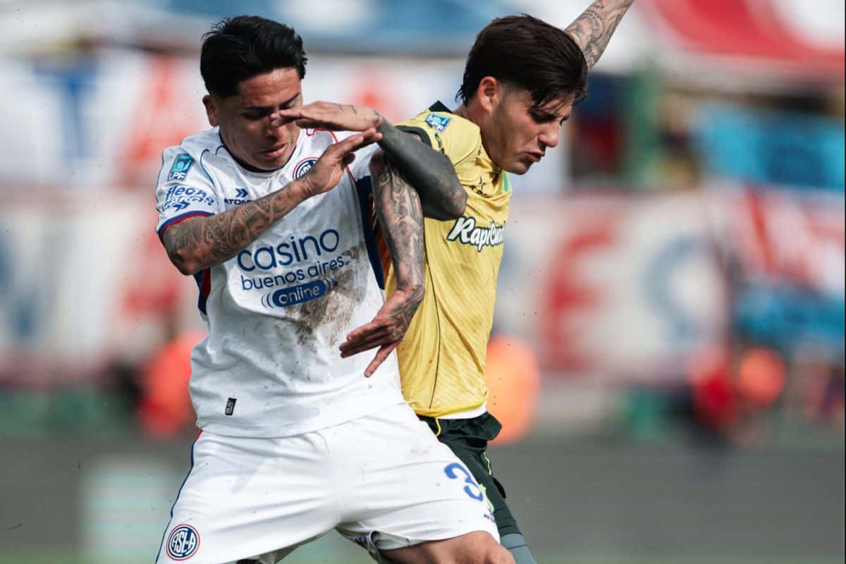 Un jugador de San Lorenzo, de camiseta blanca, disputa la pelota con un futbolista de Defensa y Justicia, de amarillo, en Florencio Varela