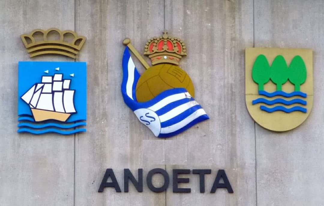 El cartel del estadio de Anoeta, en San Sebastián, con los escudos de la ciudad, de la Real Sociedad y de Gipuzkoa sobre una pared de hormigón; foto de archivo de 2022 (foto: Zarateman, Wikimedia Commons, dominio público CC0)
