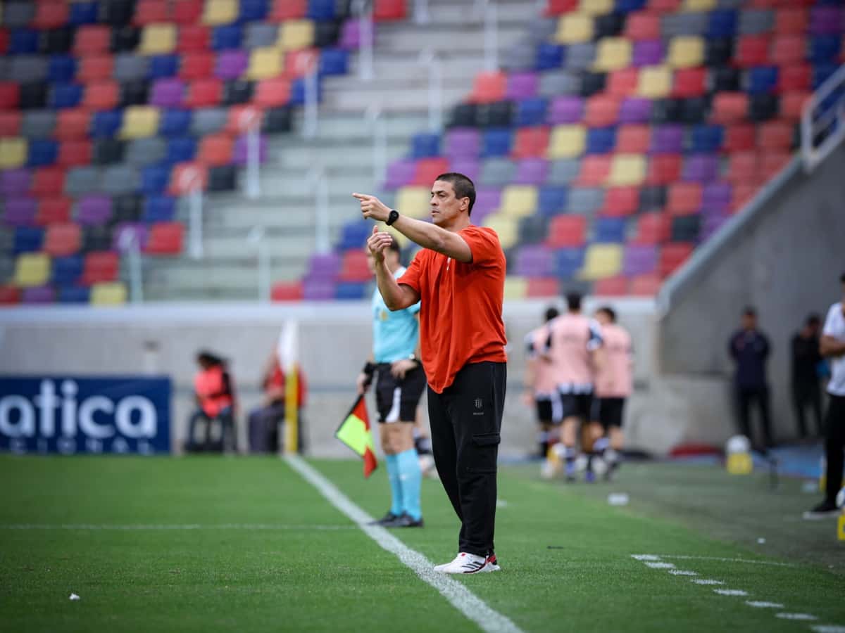 Alexander Medina, entrenador de Estudiantes, con remera naranja, da indicaciones con el brazo extendido junto a la línea de cal en el estadio Madre de Ciudades, durante el empate 2-2 con Central Córdoba (foto: prensa oficial de Estudiantes de La Plata)