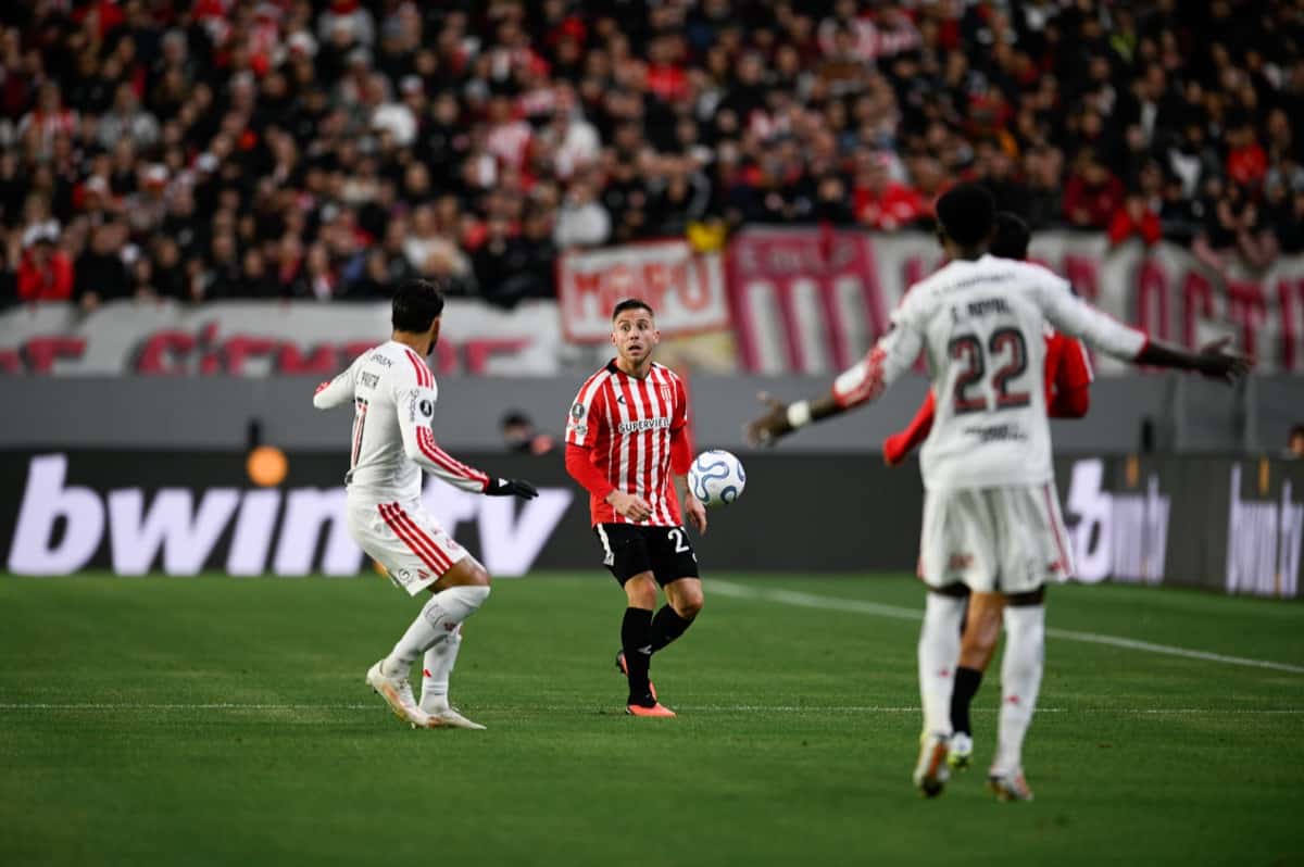 Un jugador de Estudiantes, con la camiseta albirroja, controla la pelota entre futbolistas de Flamengo de blanco, entre ellos Emerson Royal con el número 22, en el estadio UNO de La Plata durante la ida de la semifinal de la Libertadores (foto: prensa oficial de Estudiantes de La Plata)