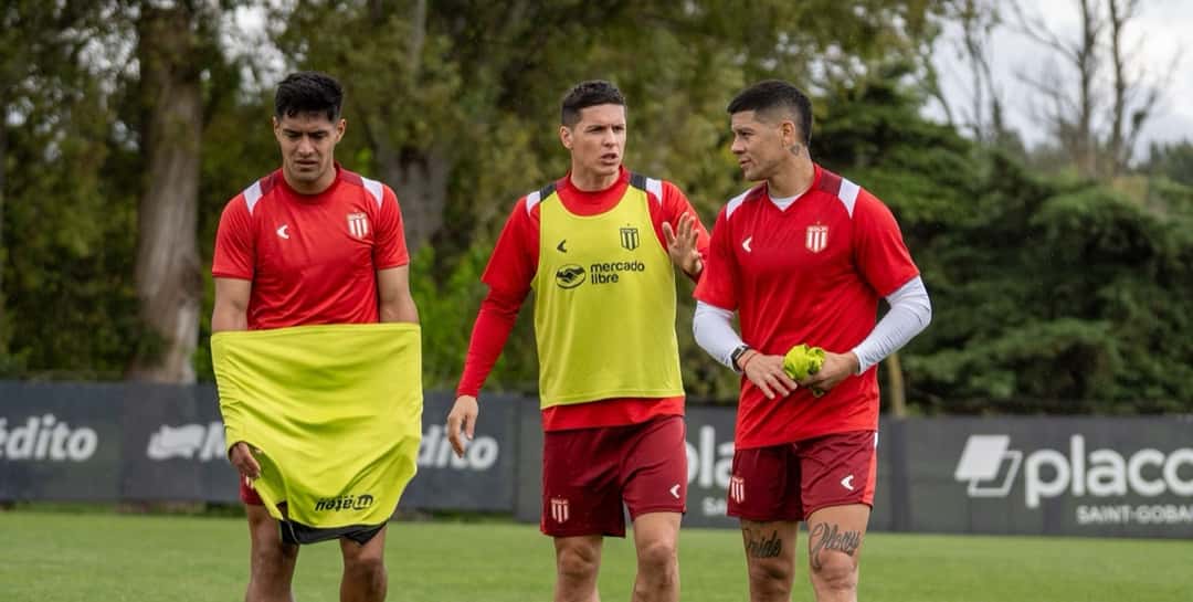 Tres jugadores de Estudiantes, con la ropa de entrenamiento roja del club y uno de ellos con pechera amarilla, caminan por el predio durante una práctica; foto de archivo de octubre (foto: prensa Estudiantes de La Plata)