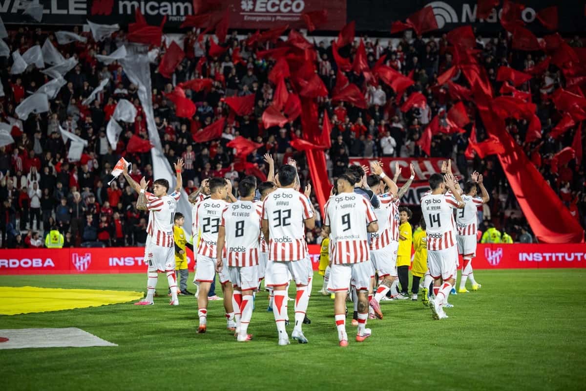 Los jugadores de Instituto, con la camiseta blanca y roja, saludan a su gente antes de un partido en Alta Córdoba, con la tribuna llena de banderas rojas (foto de archivo de agosto de 2026: prensa oficial de Instituto)