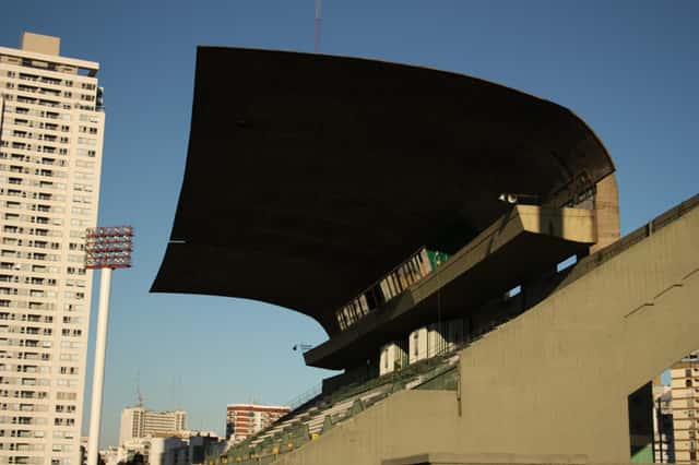 El techo curvo de la platea del estadio de Ferro, de hormigón, recortado contra el cielo azul con edificios de Caballito detrás; foto de archivo de 2012 (foto: Facundo Diez, Wikimedia Commons, licencia CC BY-SA 3.0)