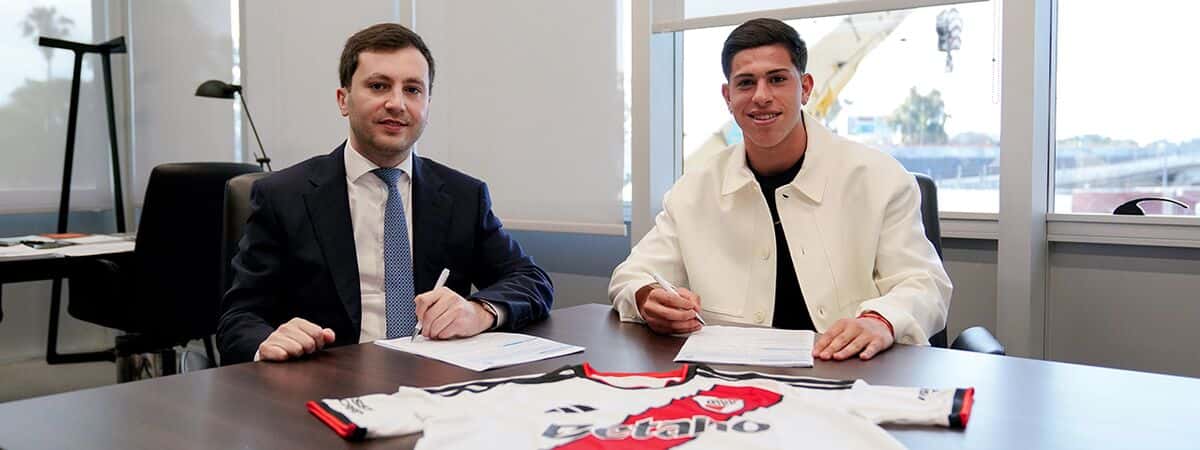 Lautaro Pereyra, con campera blanca, firma su nuevo contrato en una oficina del Monumental junto al presidente de River, Stefano Di Carlo, con la camiseta del club sobre la mesa (foto: prensa River Plate)