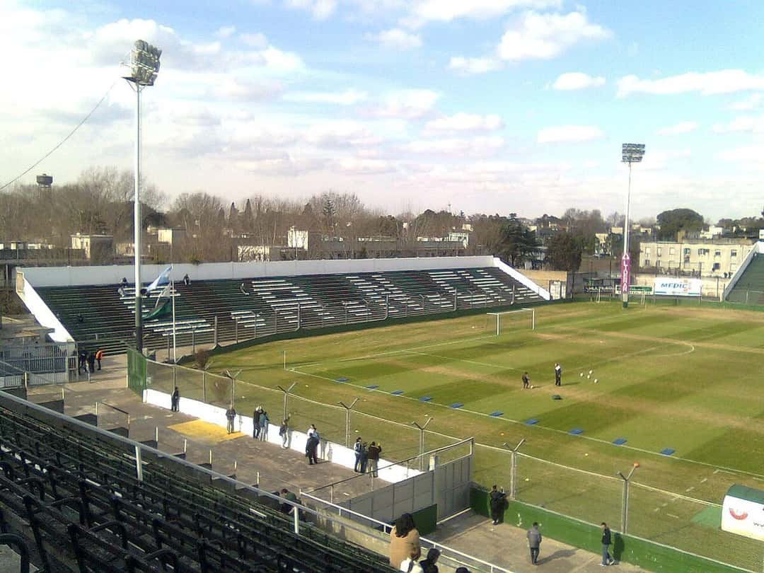 La cabecera del estadio República de Mataderos, con las tribunas verdes y negras y los árboles del barrio de fondo, vista desde la platea; foto de archivo (foto: Herjherrera, Wikimedia Commons, dominio público)