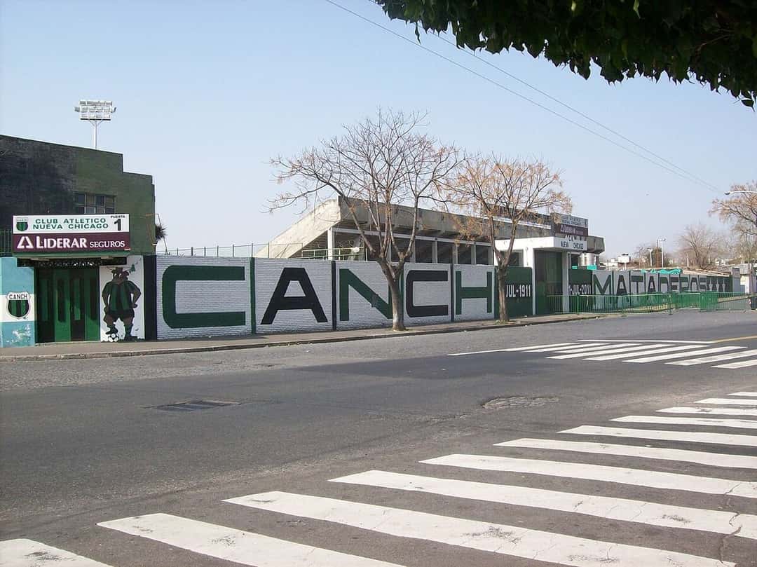 El frente del estadio de Nueva Chicago sobre la calle, con el paredón verde y blanco que dice «La cancha» y el escudo del club; foto de archivo (foto: Herjherrera, Wikimedia Commons, dominio público)