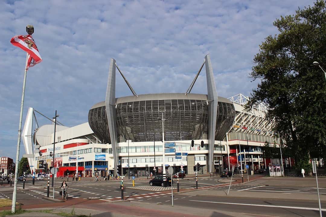 El Philips Stadion visto desde una esquina de la calle, con la bandera del PSV en un mástil; foto de archivo de julio de 2013 (foto: Metro Centric, Wikimedia Commons, licencia CC BY 2.0)