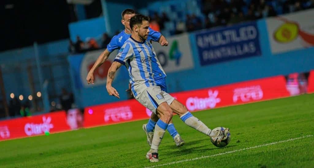 Un jugador de Racing, con la camiseta albiceleste, juega la pelota ante la marca de un rival de Estudiantes de Río Cuarto en el estadio Antonio Candini (foto: Racing Club)
