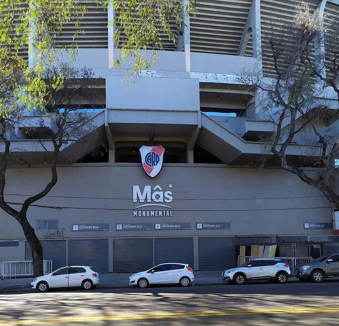 La entrada del estadio Monumental, con el escudo de River y el nombre del estadio sobre la fachada gris, desde la calle; foto de archivo de agosto de 2026 (foto: Fernando Martello, Wikimedia Commons, licencia CC BY-SA 4.0)