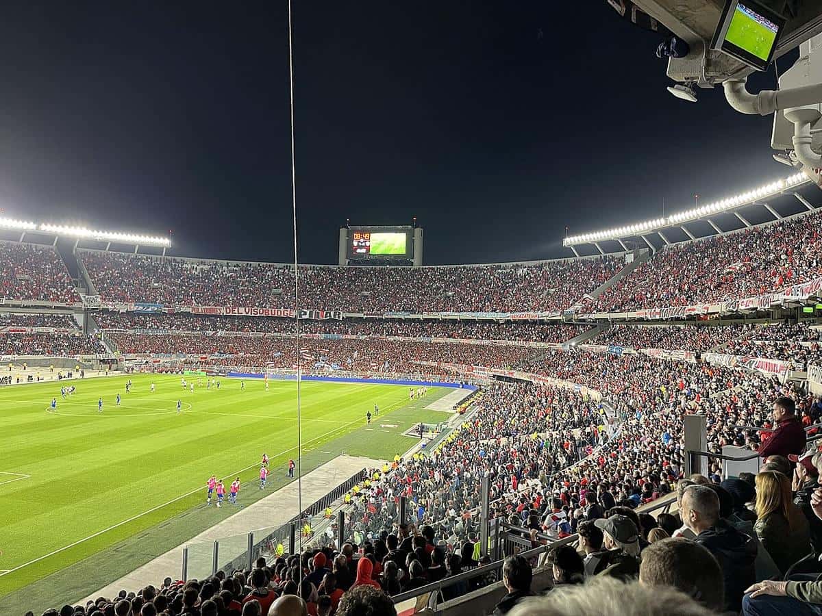 Las tribunas del Monumental llenas de hinchas de River durante un partido nocturno, con la cancha iluminada y la pantalla del estadio; foto de archivo de marzo de 2023 (foto: Vincenzo.togni, Wikimedia Commons, licencia CC BY 4.0)