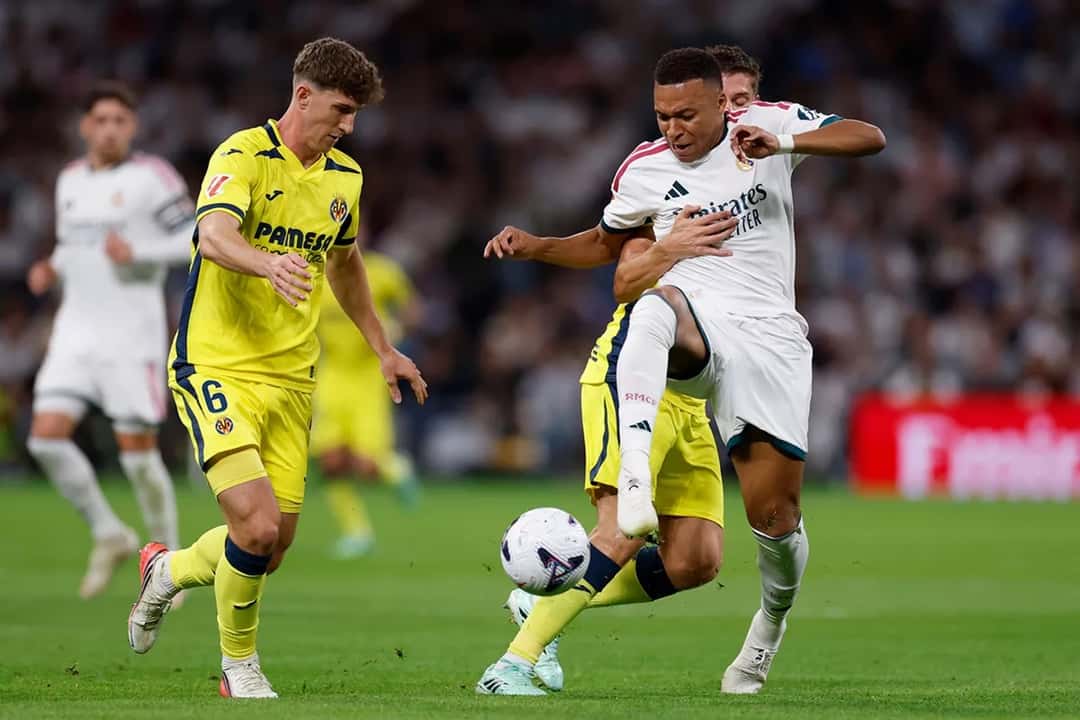 Kylian Mbappé protege la pelota entre dos jugadores del Villarreal, de camiseta amarilla, durante el partido en el Bernabéu (foto: Real Madrid C.F.)