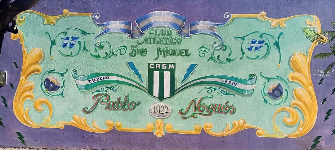 Un mural del Club Atlético San Miguel pintado en fileteado porteño, con el escudo verde y blanco, la leyenda «Trueno Verde», el año 1922 y el nombre de Pablo Nogués; foto de archivo de 2026 (foto: Mister Roboto, Wikimedia Commons, licencia CC BY-SA 4.0)