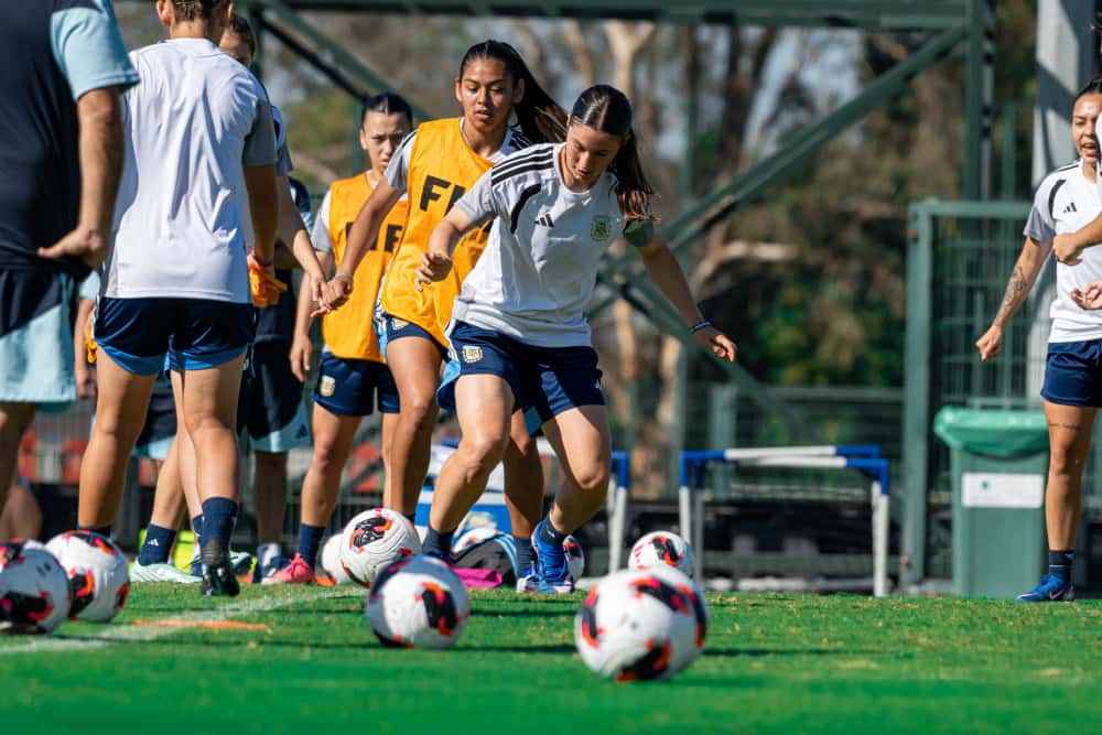 Jugadoras de la Selección argentina femenina Sub-17, con ropa de entrenamiento blanca y pecheras naranjas, hacen un ejercicio con pelotas en el entrenamiento previo a los octavos de final del Mundial (foto: prensa oficial de la AFA)