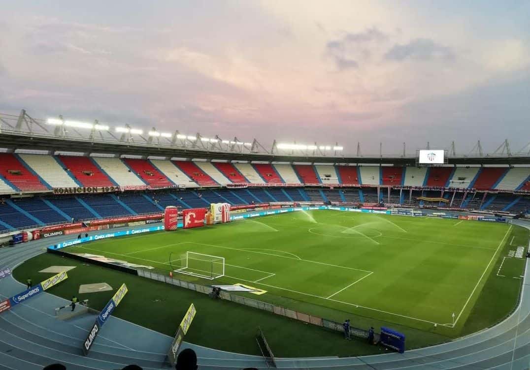 El estadio Metropolitano Roberto Meléndez, de Barranquilla, visto desde lo alto de una tribuna, con la cancha vacía y las gradas rojas y azules; foto de archivo de marzo de 2021 (foto: Bryantalv, Wikimedia Commons, licencia CC BY-SA 4.0)