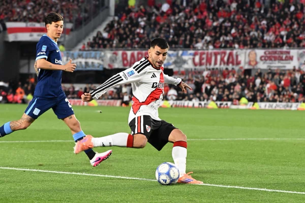 Un jugador de River, con la camiseta blanca con la banda roja, le pega a la pelota ante la marca de un jugador de Racing, de camiseta azul, con la tribuna llena del Monumental detrás; foto de archivo de octubre de 2026 (foto: prensa Liga Profesional de Fútbol)