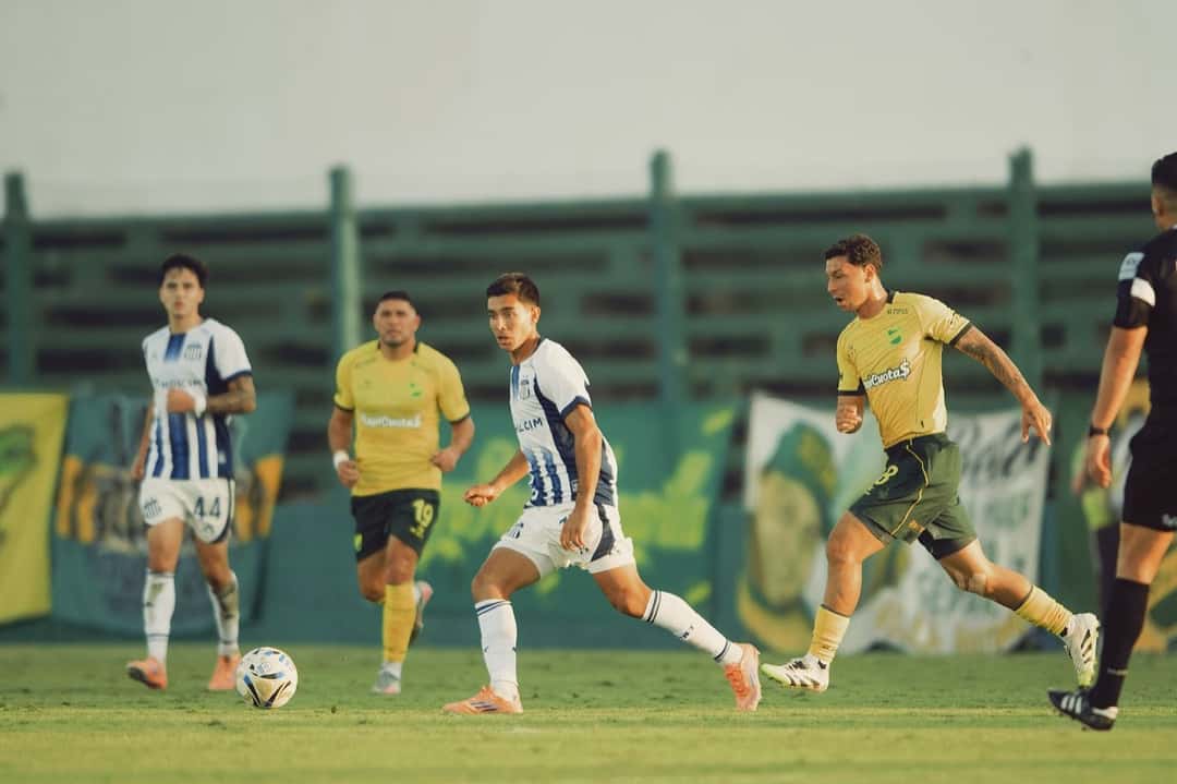 Un jugador de Talleres, con la camiseta azul y blanca, conduce la pelota con dos rivales de Defensa y Justicia, de amarillo, cerca; foto de archivo del partido entre los dos equipos en el Apertura 2026 (foto: prensa Club Atlético Talleres)