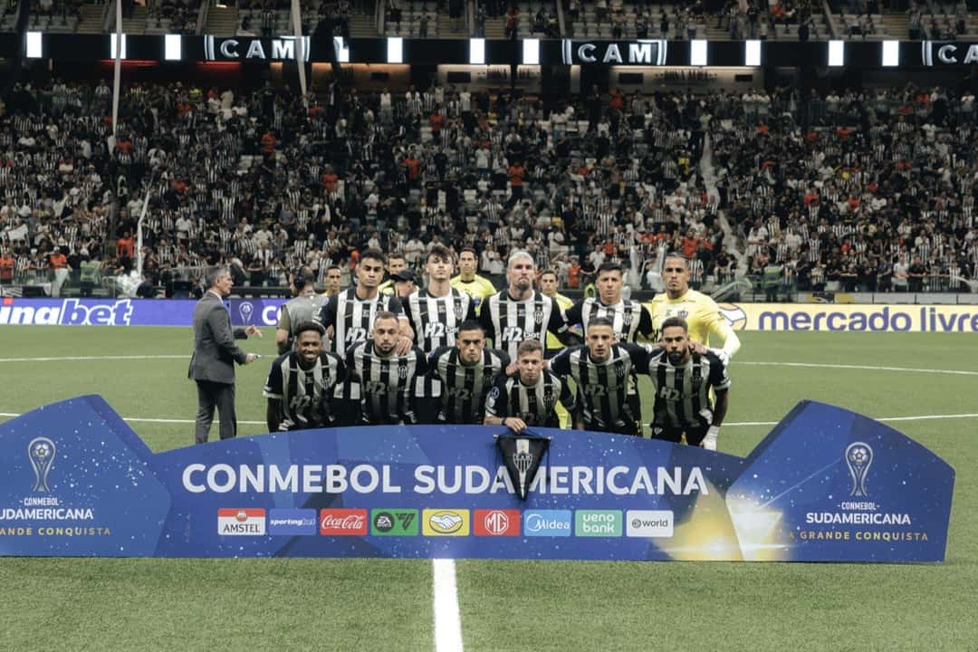 El equipo titular de Atlético Mineiro, con la camiseta a rayas blancas y negras, posa detrás del cartel de la CONMEBOL Sudamericana en la Arena MRV, con las tribunas llenas; foto de archivo (foto: Pedro Souza / prensa oficial de Atlético Mineiro)