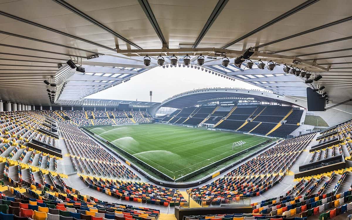 El interior del estadio del Udinese, en Udine, con sus butacas de colores, el techo curvo sobre la tribuna principal y la cancha regada; foto de archivo de enero de 2016 (foto: Matteo.favi, Wikimedia Commons, licencia CC BY-SA 4.0)