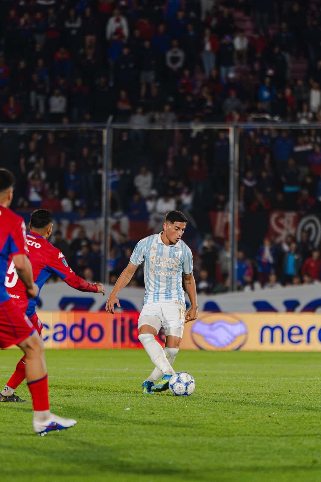 Un jugador de Atlético Tucumán, con la camiseta celeste y blanca, maneja la pelota ante la marca de dos jugadores de Tigre en el estadio de Victoria (foto: prensa Liga Profesional de Fútbol)
