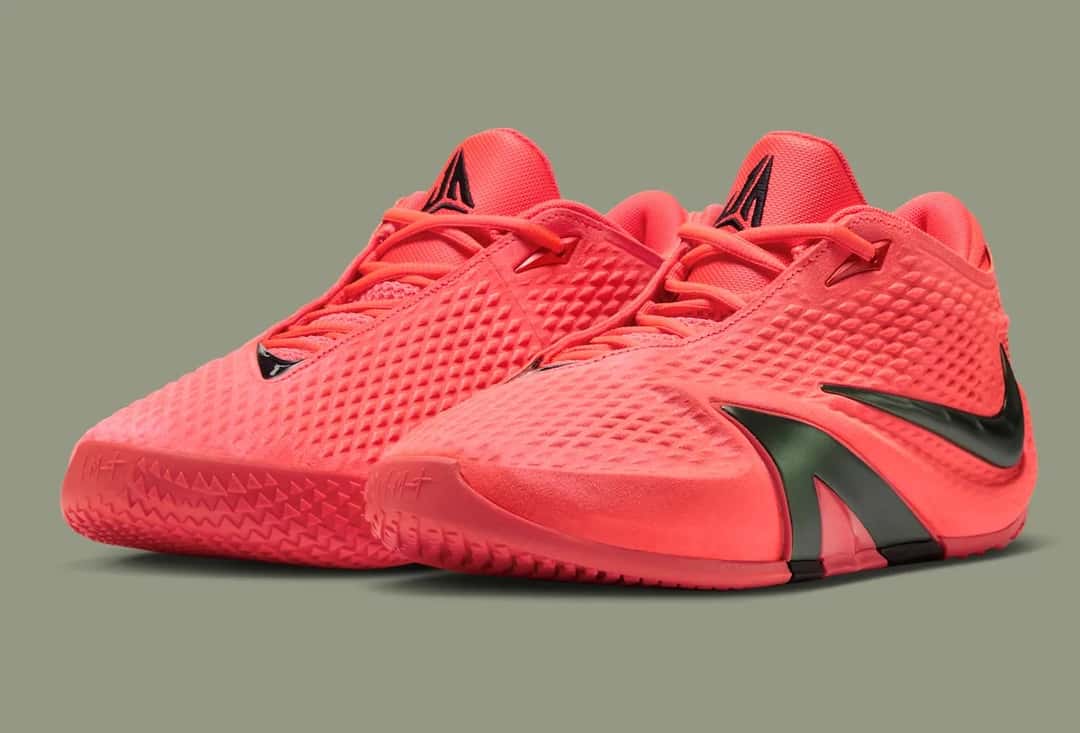 Par de Nike Ja 4 Code Red en diagonal, con la capellada roja coral texturada y las piezas oscuras en el costado, sobre fondo verde grisáceo