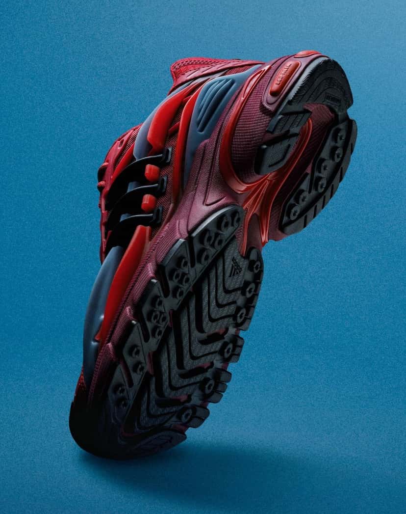 Pharrell x adidas Adistar Jellyfish Red visto desde abajo sobre fondo azul, con la suela de goma gris oscura, la mediasuela roja y bordó y las capas grises del costado