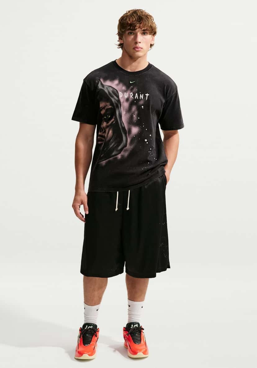 Modelo de cuerpo entero con el Nike KD 19 Halloween puesto, remera negra deslavada con la ilustración de una figura encapuchada y la palabra Durant, short de básquet negro y medias blancas Nike, sobre fondo blanco