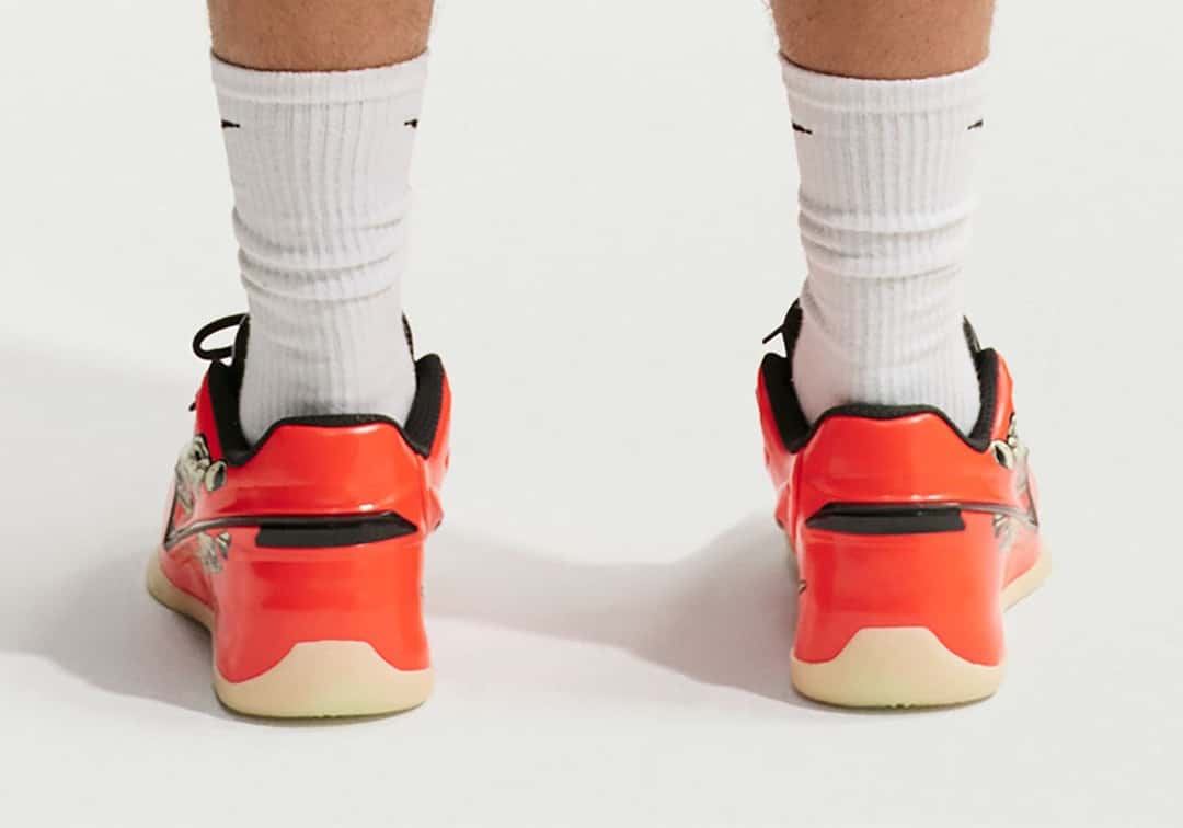 Vista trasera de un par de Nike KD 19 Halloween puestos con medias blancas Nike, con el talón naranja brillante, una franja negra horizontal, el cuello acolchado negro, parte del gráfico claro en el lateral y la suela beige semitranslúcida